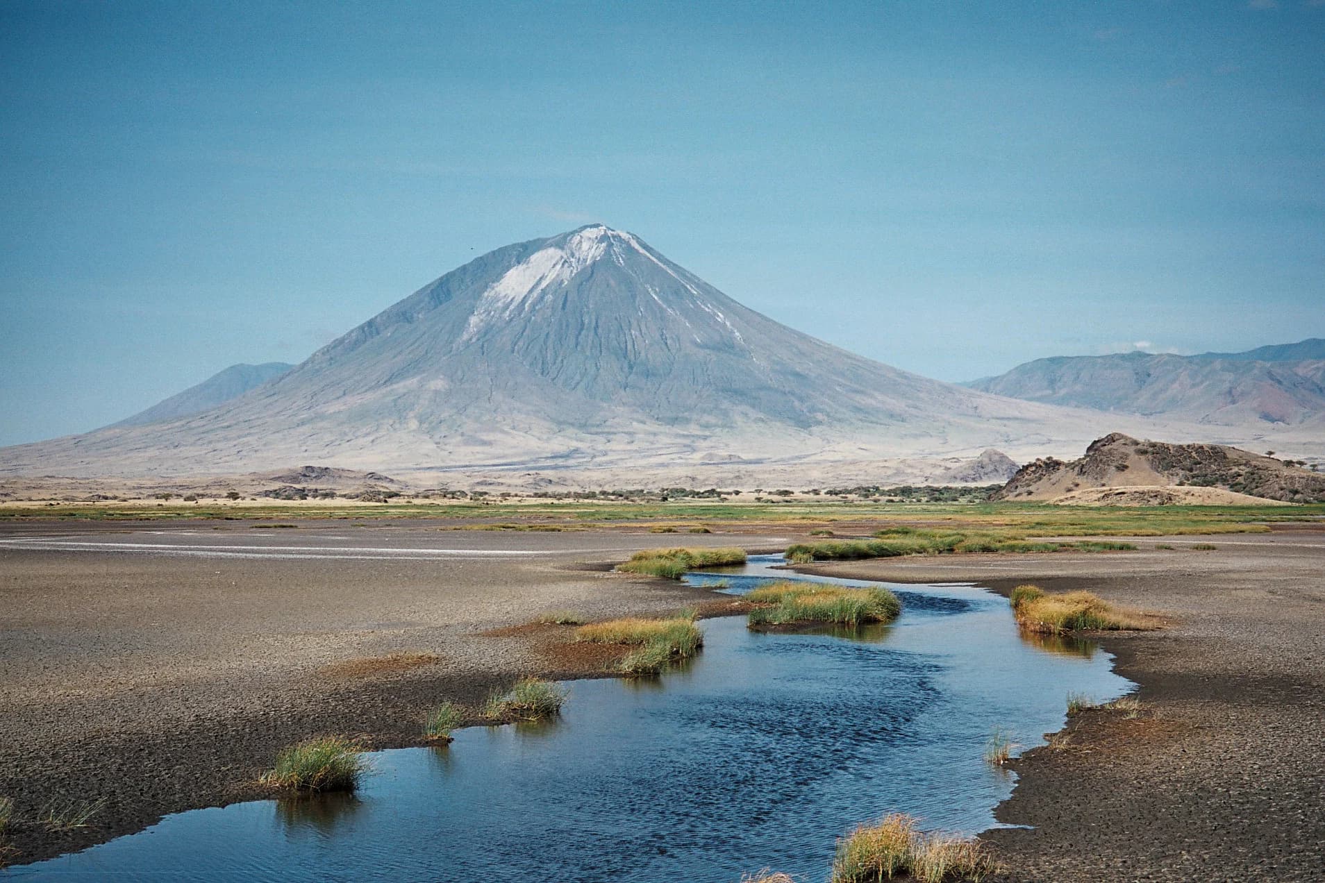 Ol Doinyo Lengai rising beyond water and volcanic plains near Lake Natron