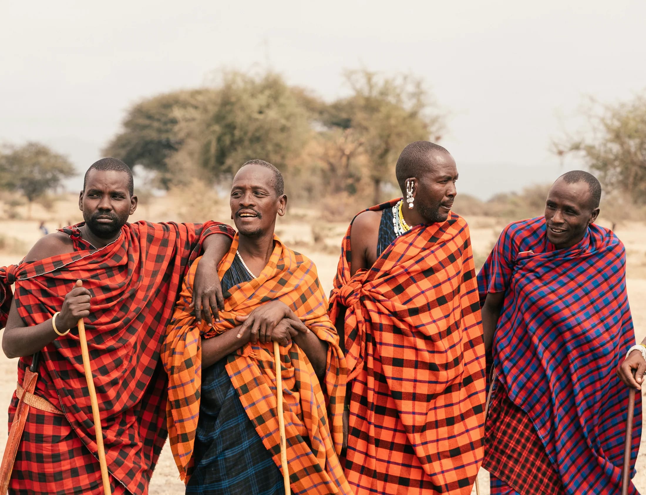 Four Maasai men in checked shukas with walking sticks in a Tanzanian village